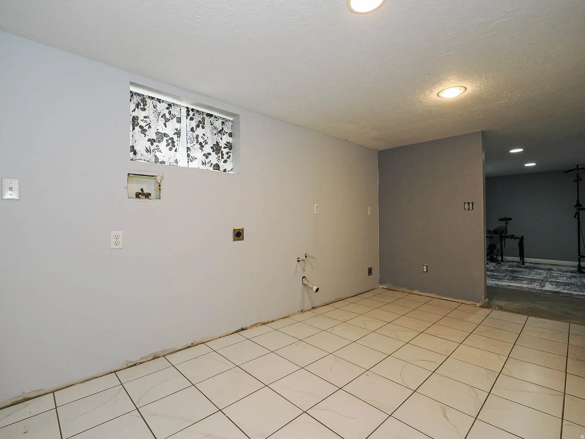 Room featuring light-toned square floor tiles, recessed ceiling lighting, and a window with a patterned curtain