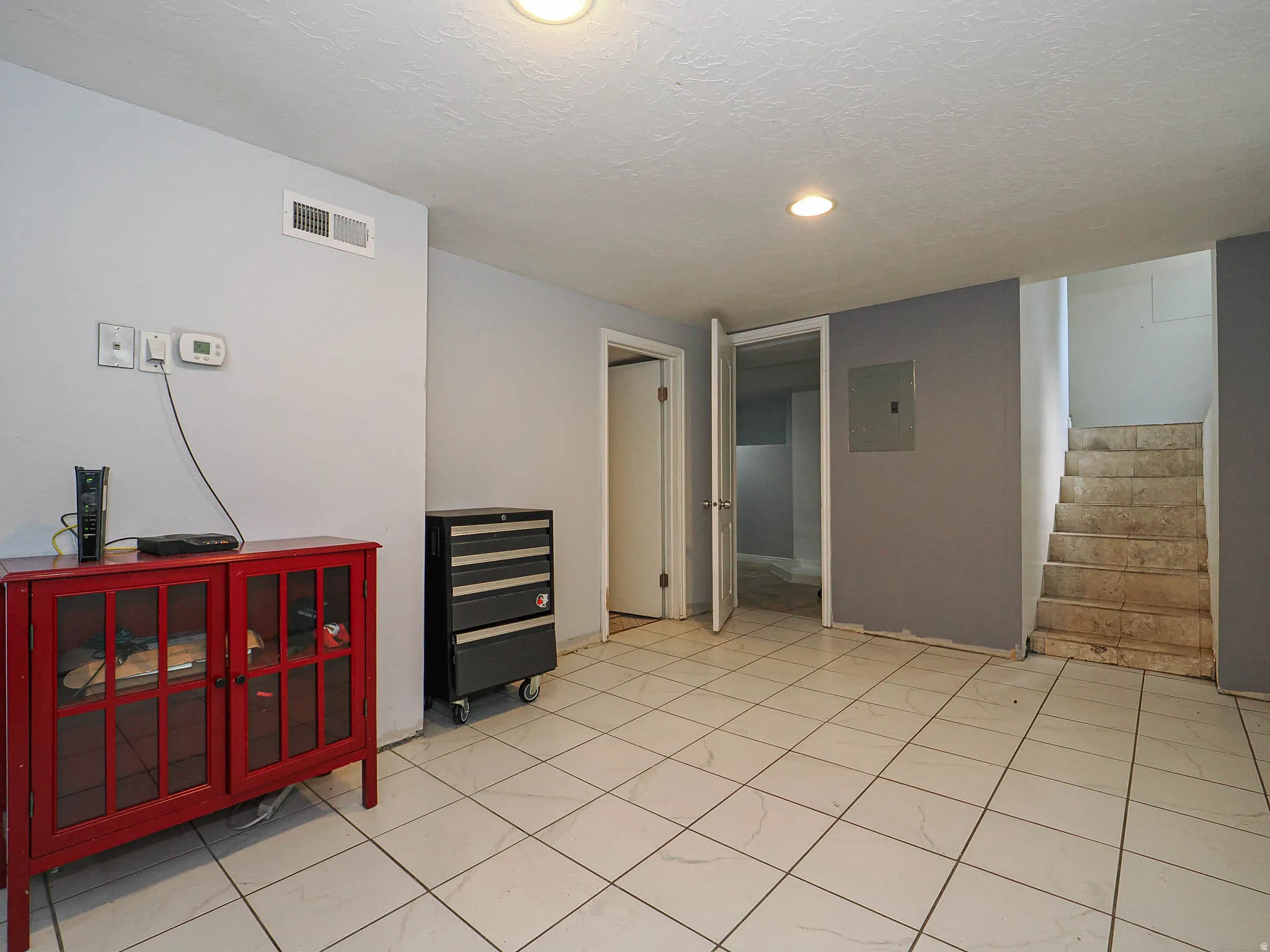Spacious room featuring white tiled flooring, light gray and dark gray wall finishes, recessed lighting, and a visible air vent