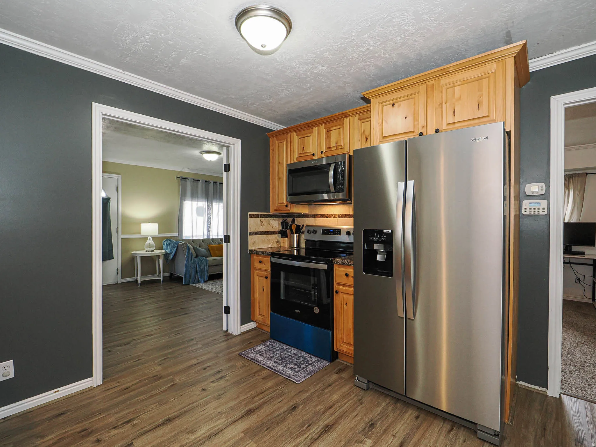 Kitchen featuring wood-finish flooring, natural wood cabinetry, stainless steel appliances, and a stone-tile backsplash