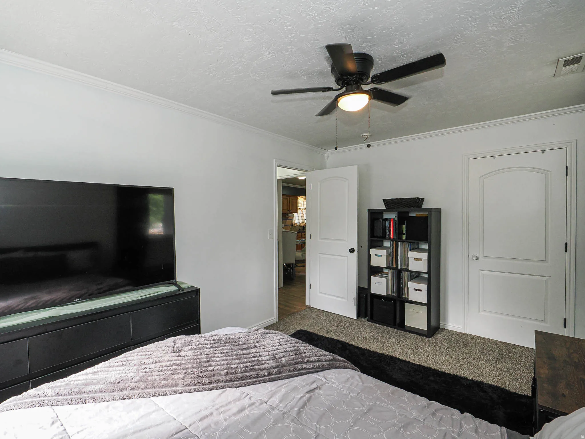 Bedroom featuring neutral wall paint, crown molding, a ceiling fan with light fixture, two panel-style doors, and carpet flooring