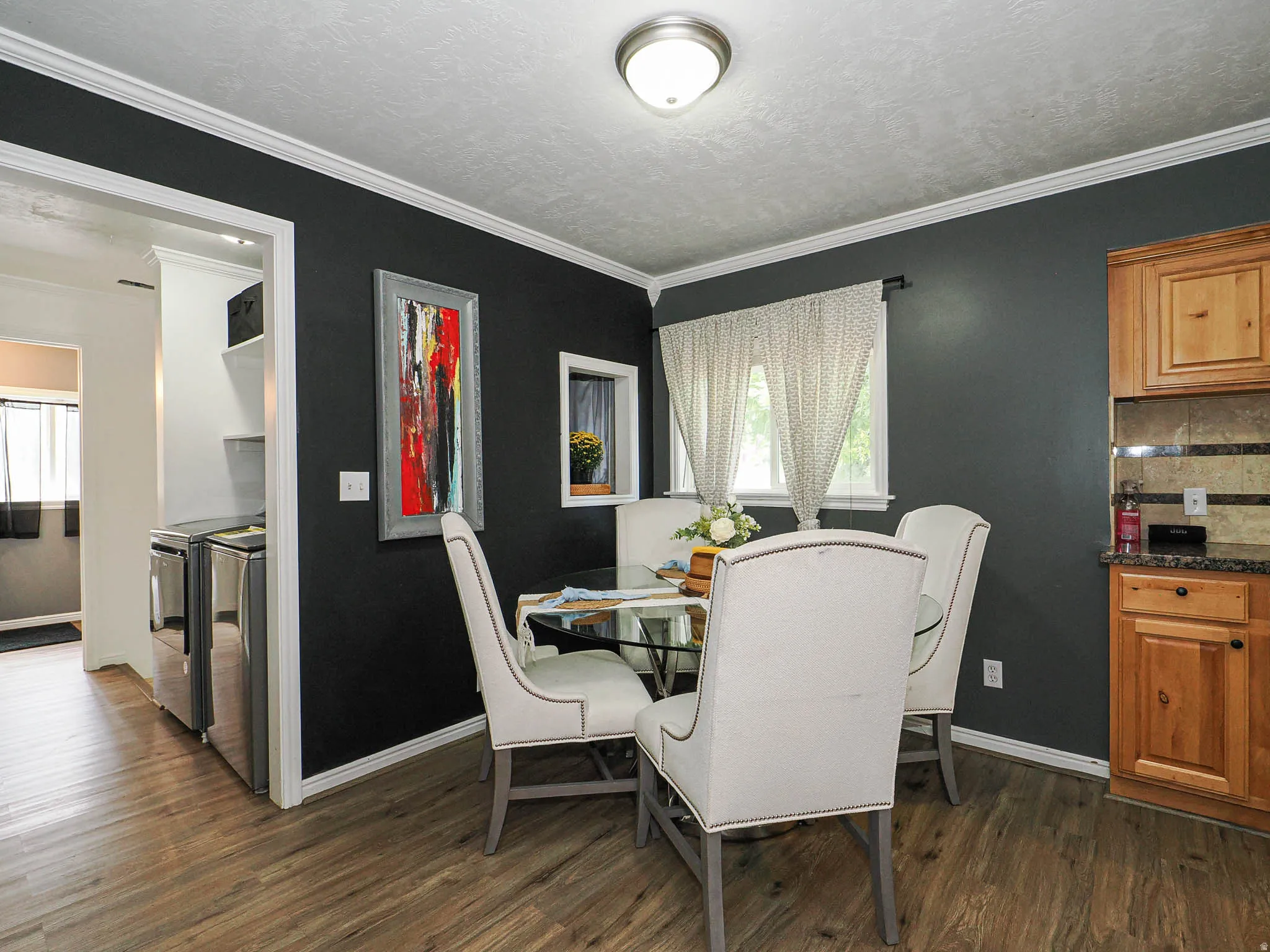 Dining area featuring wood-finish flooring, dark accent wall, white trim, and a window with natural light