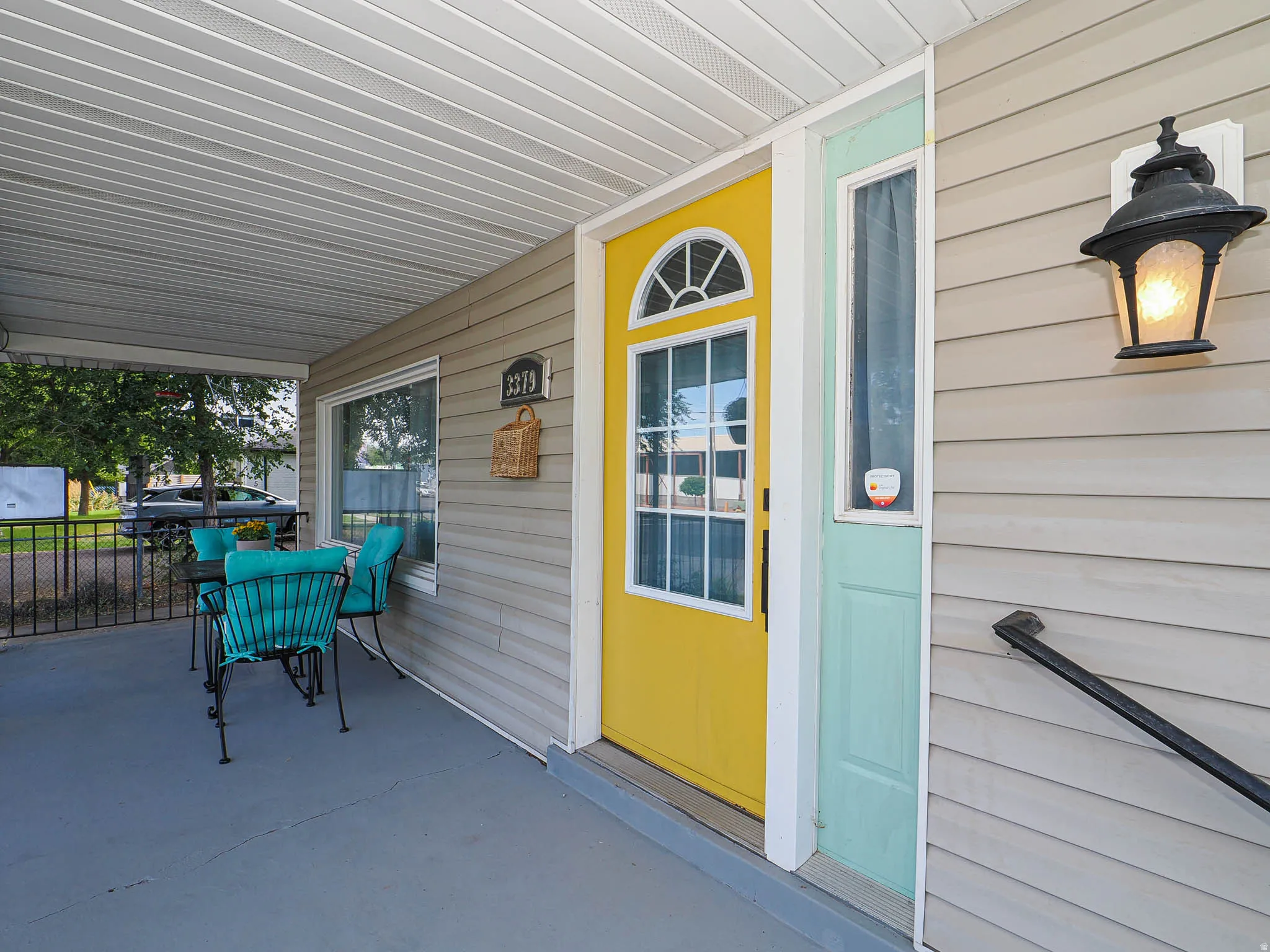 Front porch featuring light gray siding, a bright yellow entry door with an arched transom, and a side light