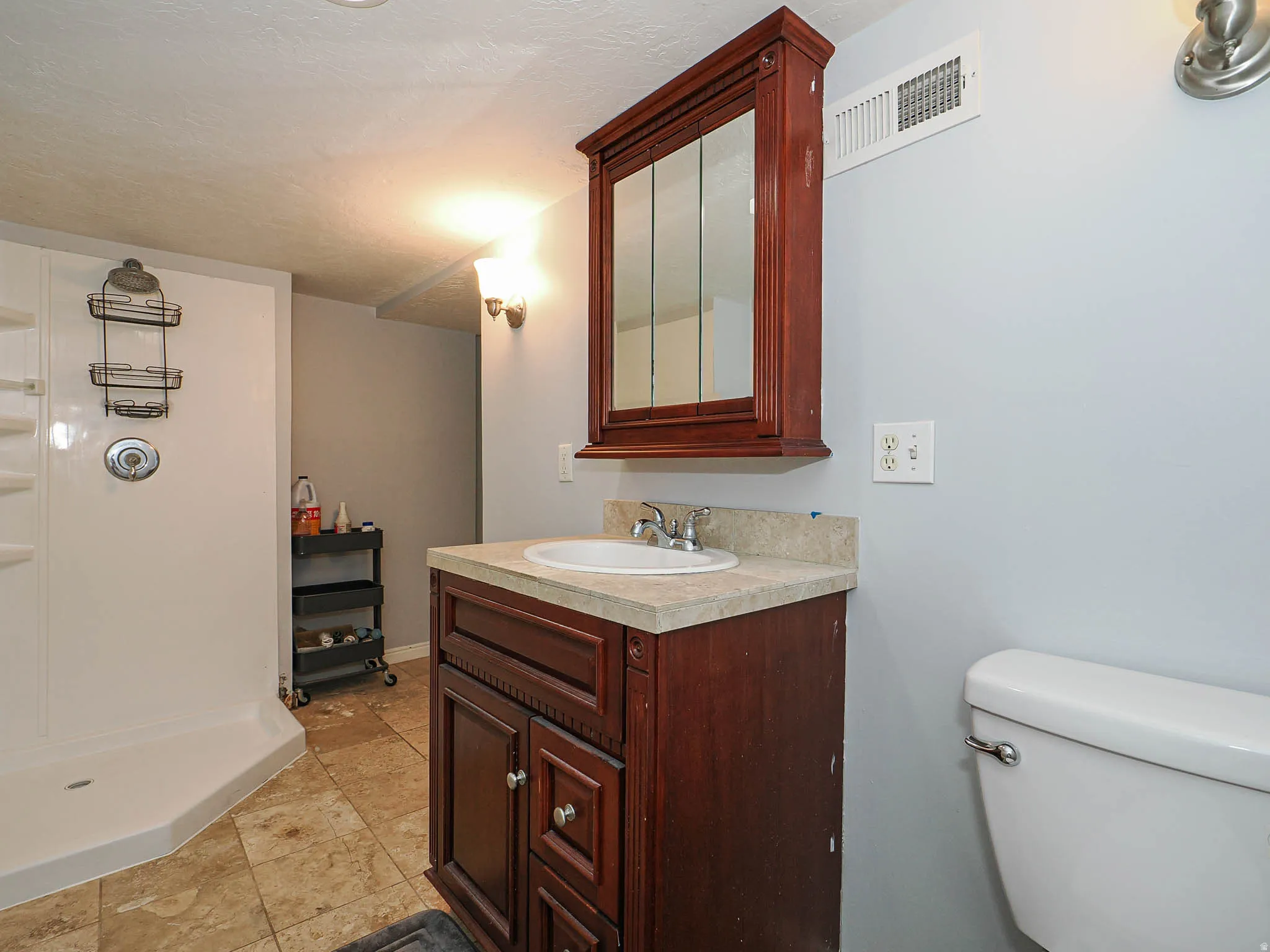 Bathroom featuring a dark wood vanity with an integrated sink, a matching mirrored medicine cabinet, a white toilet, and a stand-up shower with a chrome fixture