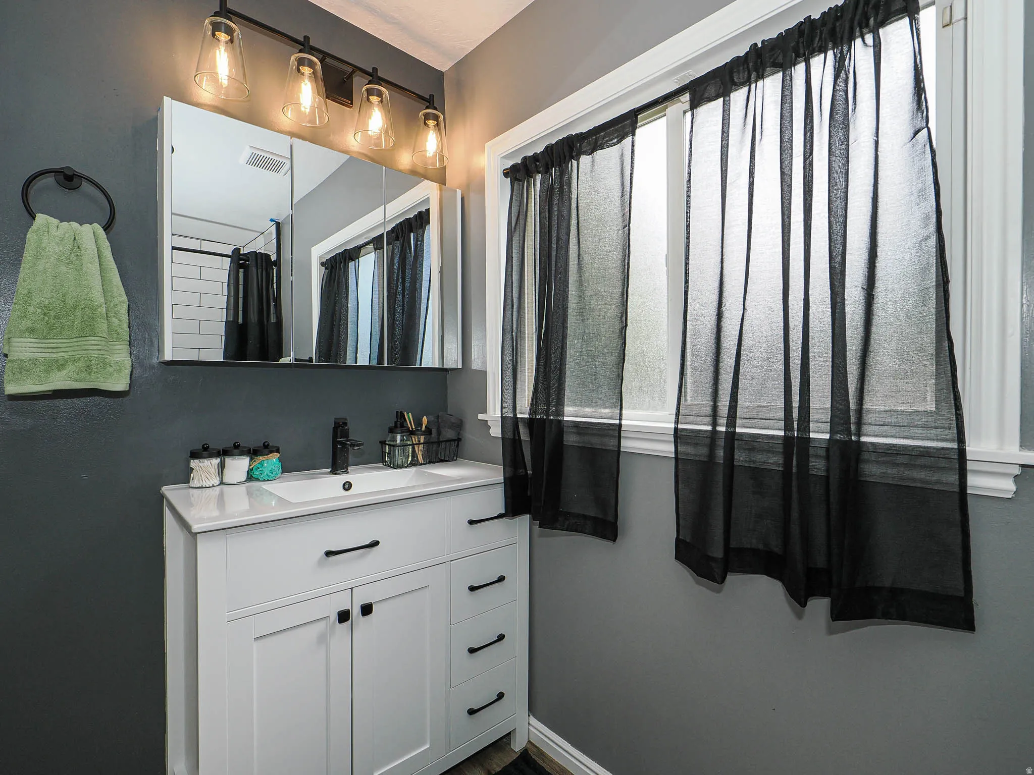 Bathroom featuring a white vanity with an integrated sink, black hardware, and a medicine cabinet with a four-light fixture