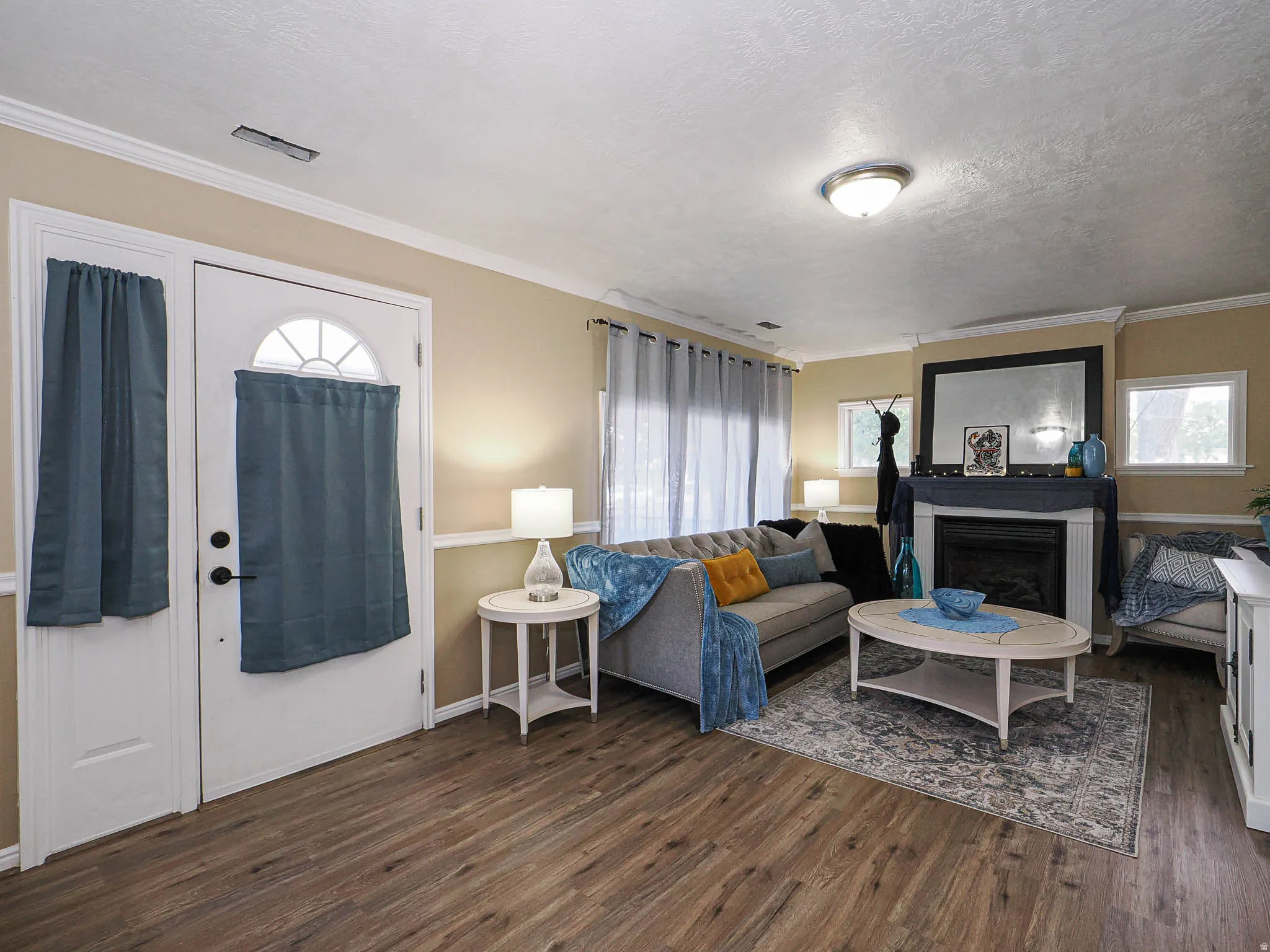 Inviting living space featuring wood-finish flooring, a white fireplace with a dark mantel, multiple windows for natural light, and a white front door with an arched window insert