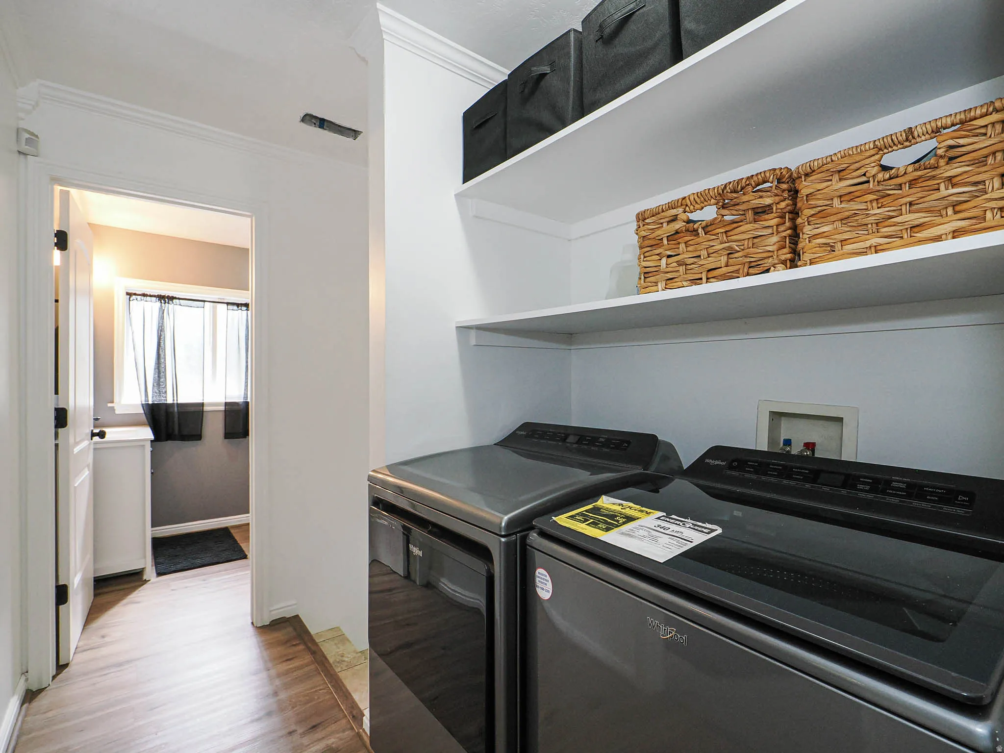 Dedicated laundry area featuring dual built-in shelving, white walls, and wood-finish flooring