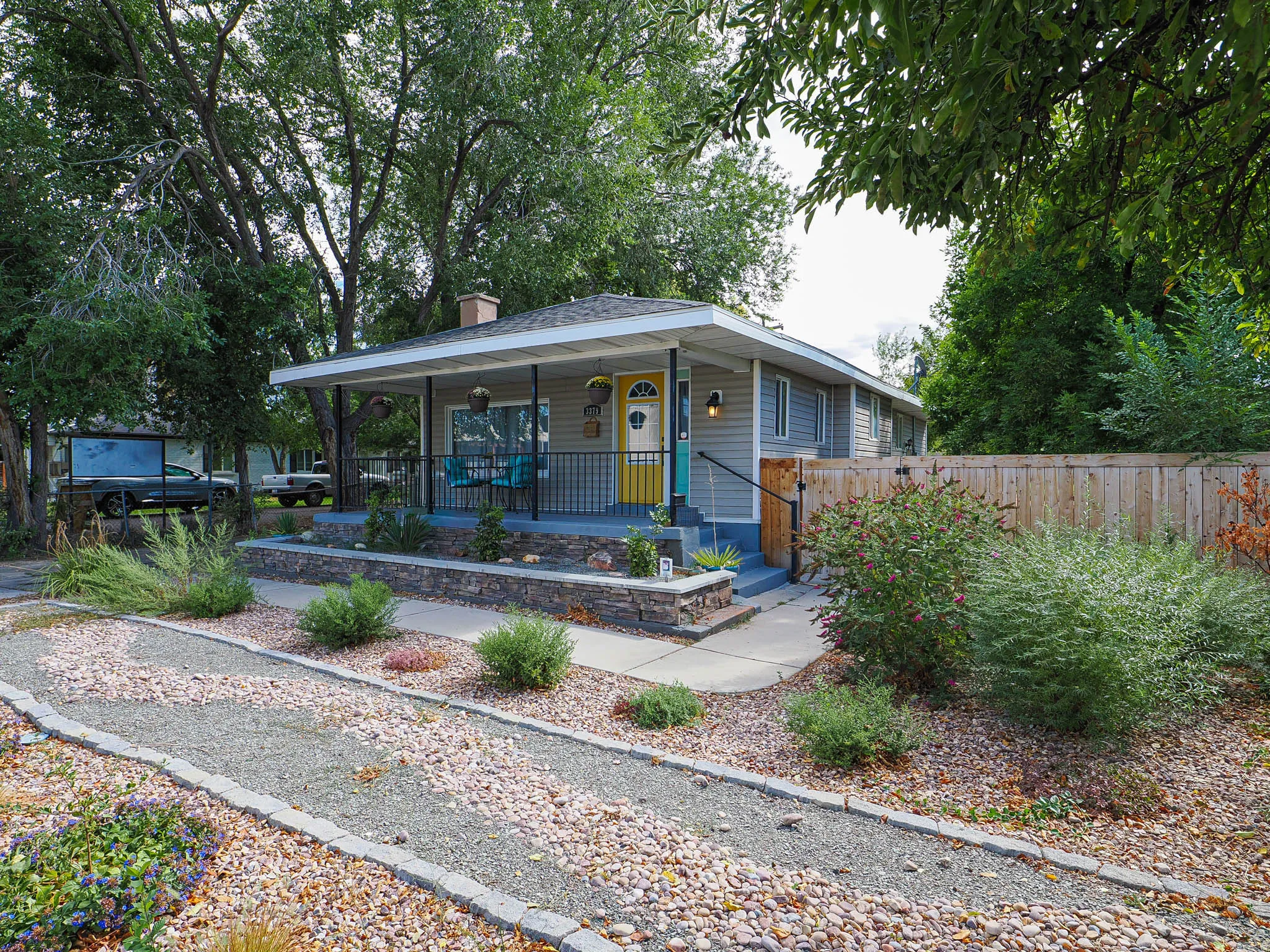 Charming single-story residence featuring a covered front porch, a bright yellow entry door, and light gray siding