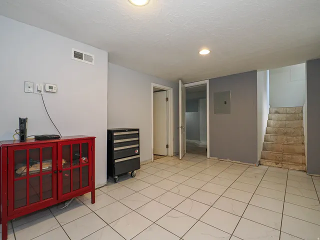 Spacious room featuring white tiled flooring, light gray and dark gray wall finishes, recessed lighting, and a visible air vent