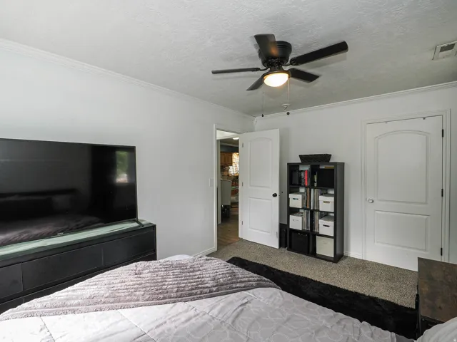 Bedroom featuring neutral wall paint, crown molding, a ceiling fan with light fixture, two panel-style doors, and carpet flooring