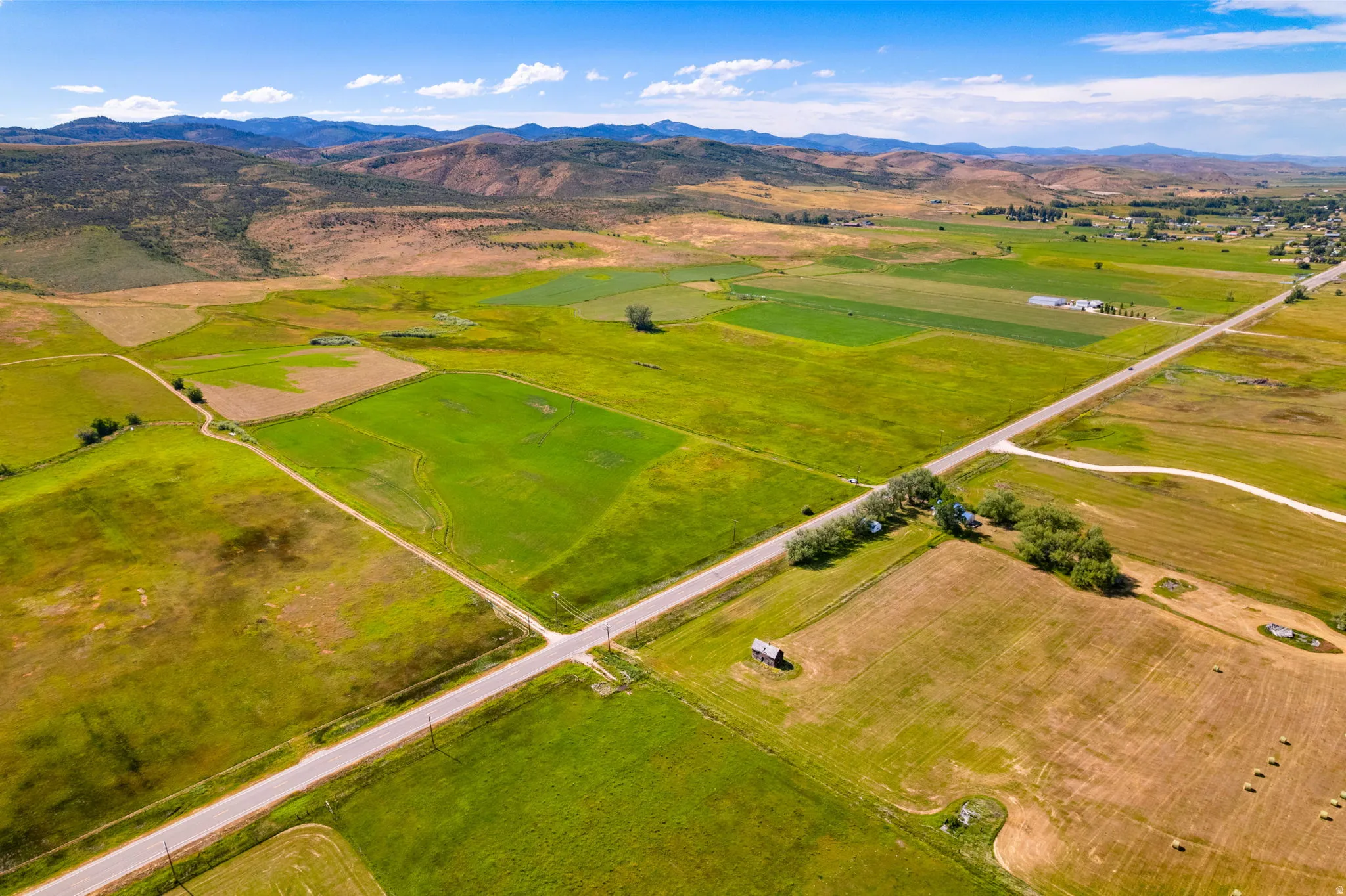 Expansive land parcel featuring diverse field patterns, a paved road, and distant mountain topography