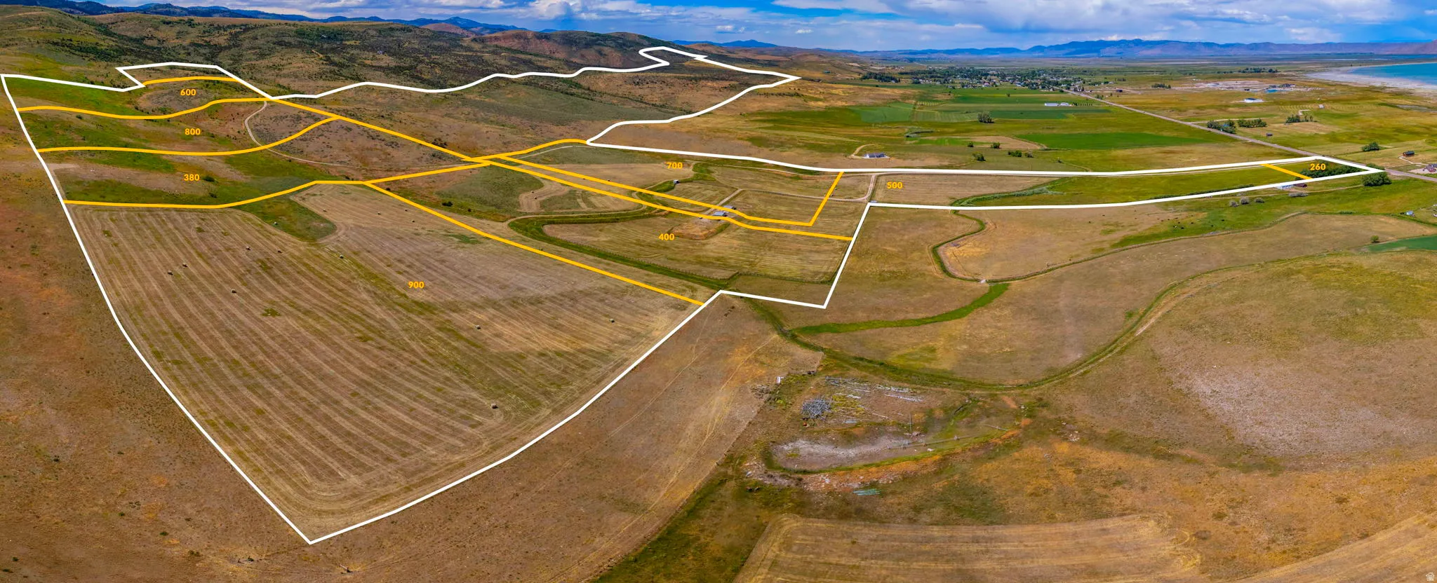 Expansive land parcel featuring delineated boundaries, varied topography, agricultural fields, and distant water frontage