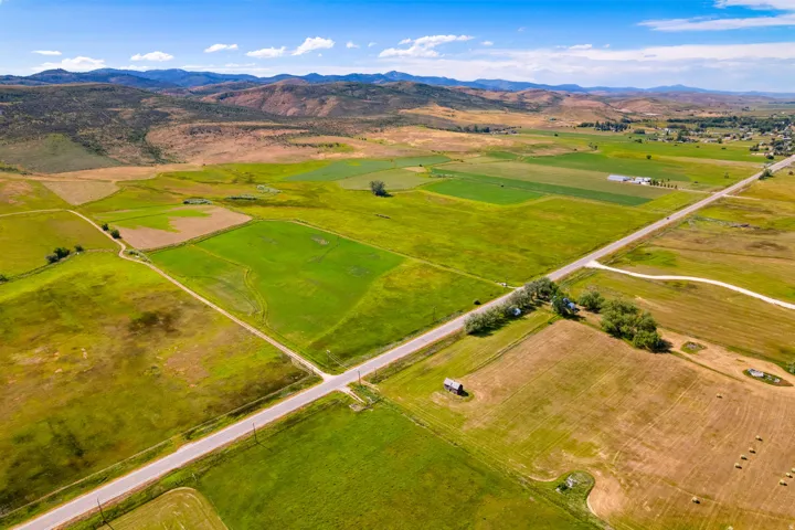 Expansive land parcel featuring diverse field patterns, a paved road, and distant mountain topography