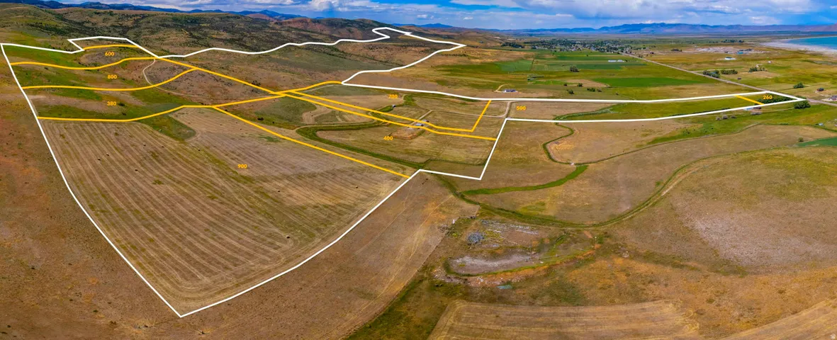 Expansive land parcel featuring delineated boundaries, varied topography, agricultural fields, and distant water frontage