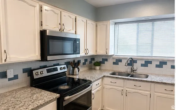 White cabinetry with dark hardware, stainless steel appliances, dual basin sink with a gooseneck faucet, light-colored countertops, and a subway tile backsplash with blue accents