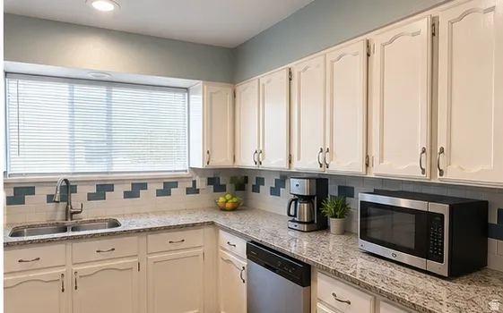 White cabinetry, dual basin stainless steel sink, patterned tile backsplash, light-toned countertops, and recessed lighting