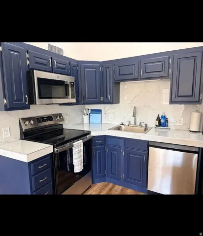 Kitchen featuring navy cabinetry with panel detailing, light-toned countertops, a stainless steel over-the-range microwave, a stainless steel electric range, and a stainless steel dishwasher