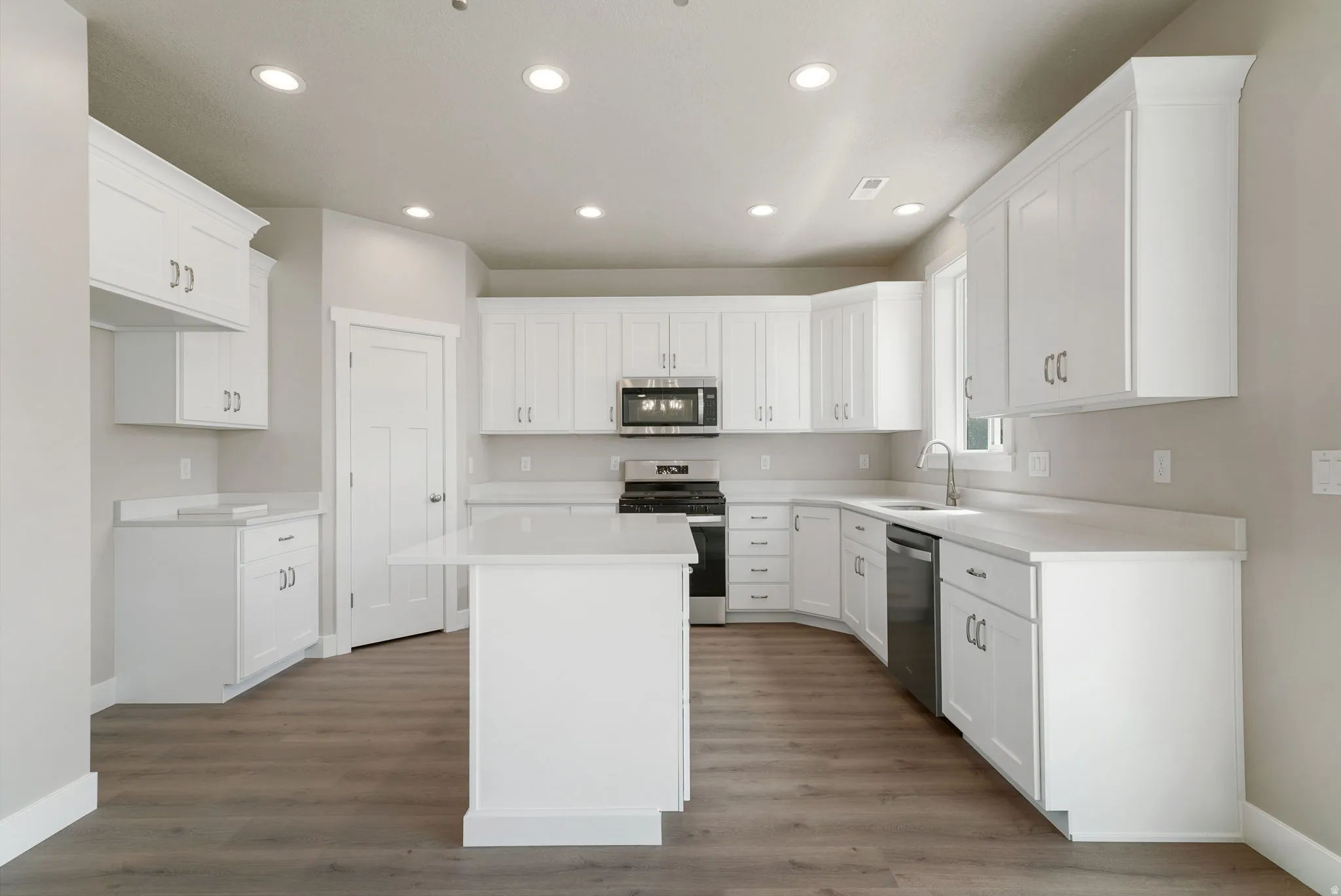 Bright kitchen featuring white cabinetry, a central island, stainless steel appliances, recessed lighting, and wood-finish flooring
