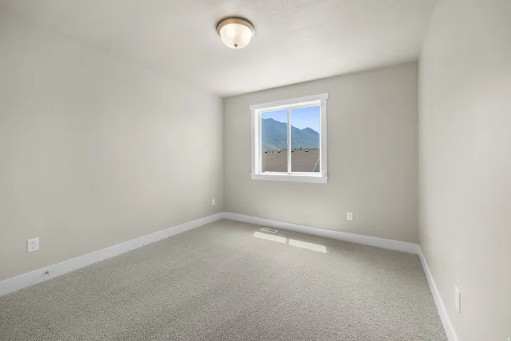 Neutral-toned walls and plush carpeting in a bright room with a single window offering a mountain backdrop