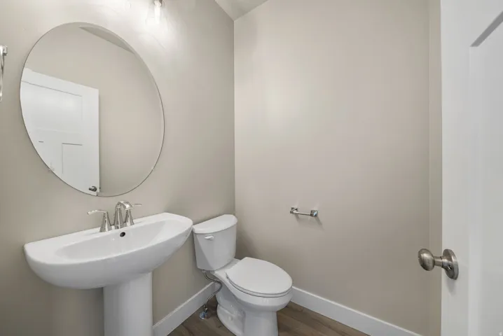 Pedestal sink with chrome faucet, complemented by an oval wall-mounted mirror and overhead lighting