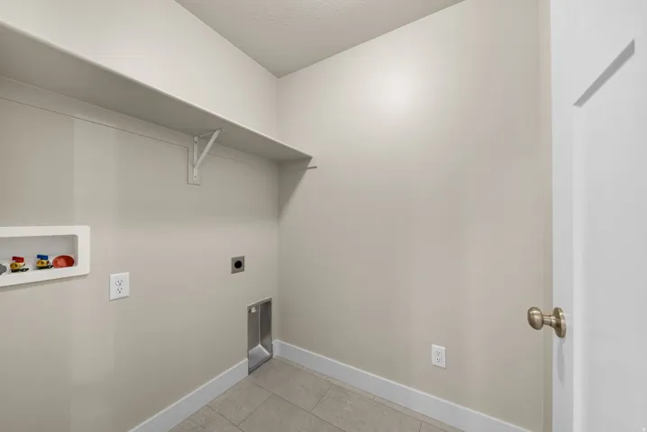 Utility space featuring neutral wall tones, durable tile flooring, and a built-in wall shelf
