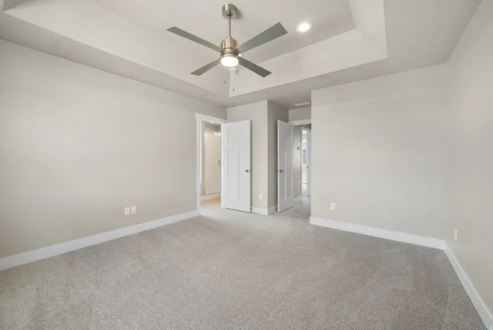 Spacious carpeted room featuring a recessed ceiling with a brushed nickel ceiling fan and integrated lighting, light neutral wall paint, and white trim molding