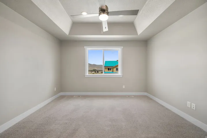 Neutral-toned room featuring a tray ceiling with a ceiling fan, carpet flooring, and white baseboards