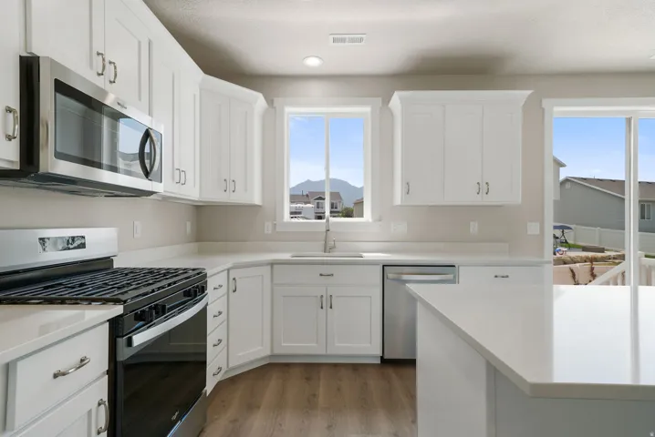 Modern kitchen featuring white shaker cabinetry, stainless steel appliances, light-toned countertops, and wood-finish flooring