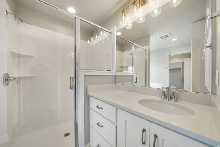 Bathroom featuring a white subway tile shower with glass enclosure, single vanity with white cabinetry, integrated sink, and a large mirror with multi-bulb light fixture