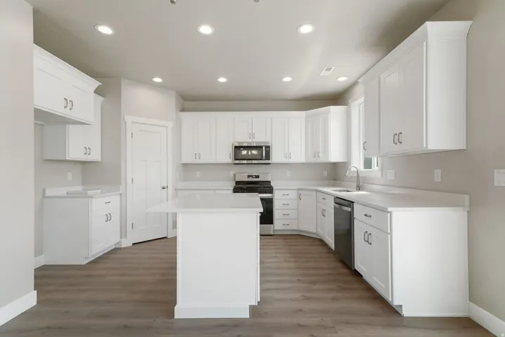 Bright kitchen featuring white cabinetry, a central island, stainless steel appliances, recessed lighting, and wood-finish flooring