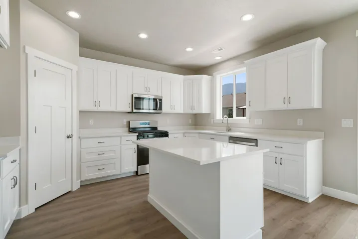 Contemporary kitchen featuring abundant white cabinetry, stainless steel appliances, a center island with countertop, wood-finish flooring, and recessed lighting