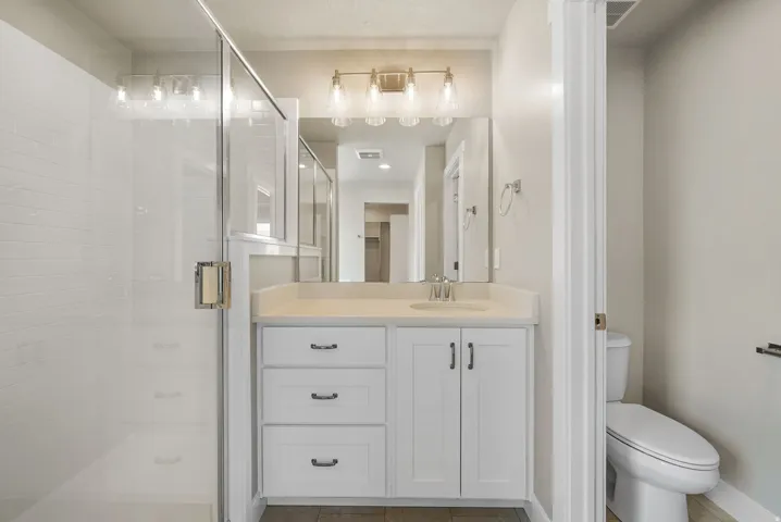 Full bathroom featuring a glass-enclosed shower with white subway tile, a vanity with a light-colored countertop, and a built-in toilet