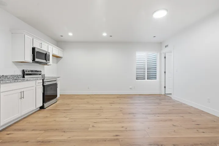Open-concept living area featuring wood-finish flooring, white cabinetry with silver hardware, stainless steel appliances, and recessed lighting