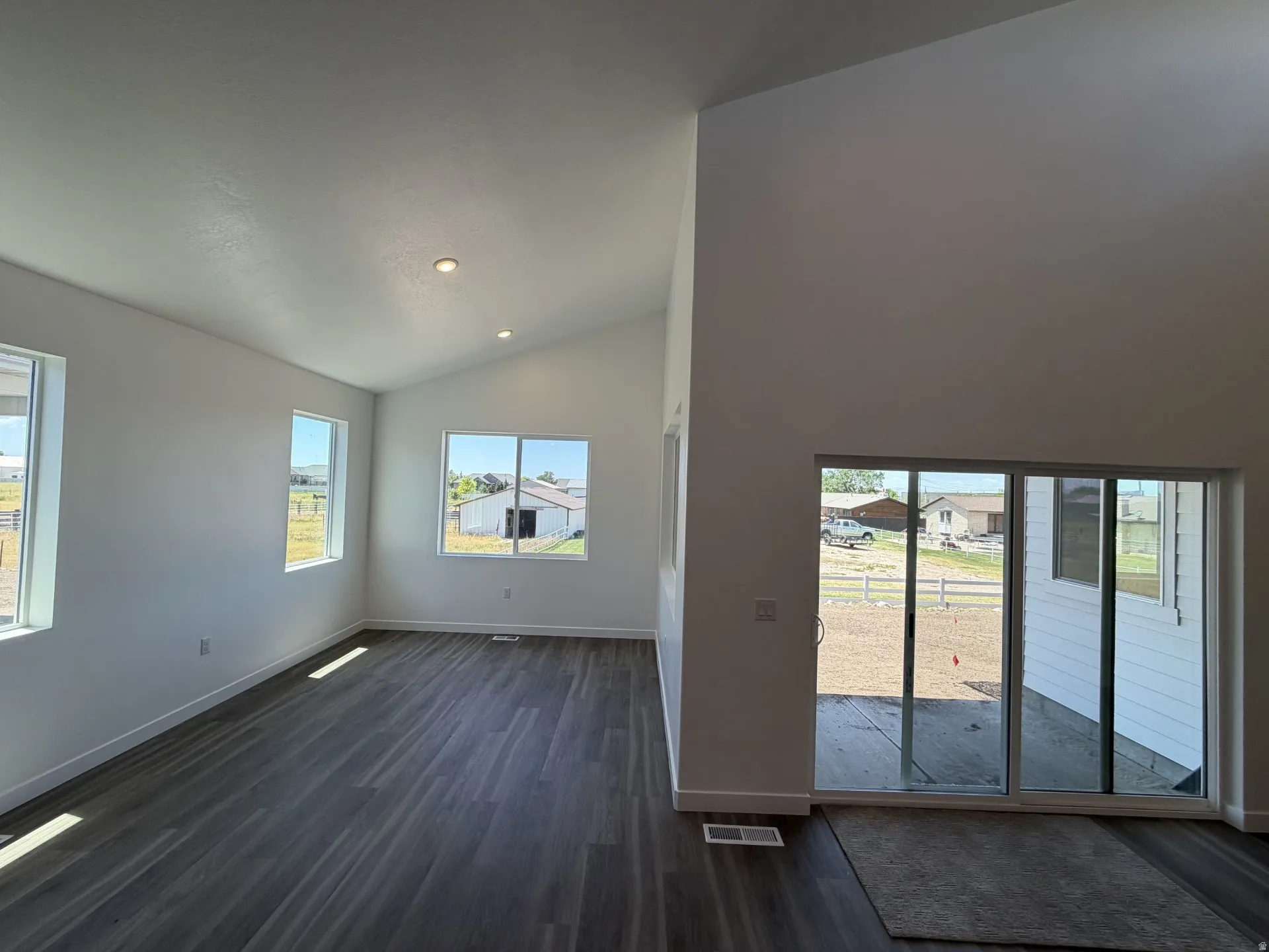 Spacious room featuring vaulted ceilings, recessed lighting, wood-finish flooring, multiple windows, and a sliding glass door