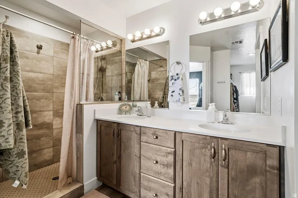 Bathroom featuring a spacious double vanity with wood-finish cabinetry and integrated sinks, complemented by two large mirrors and two overhead light fixtures
