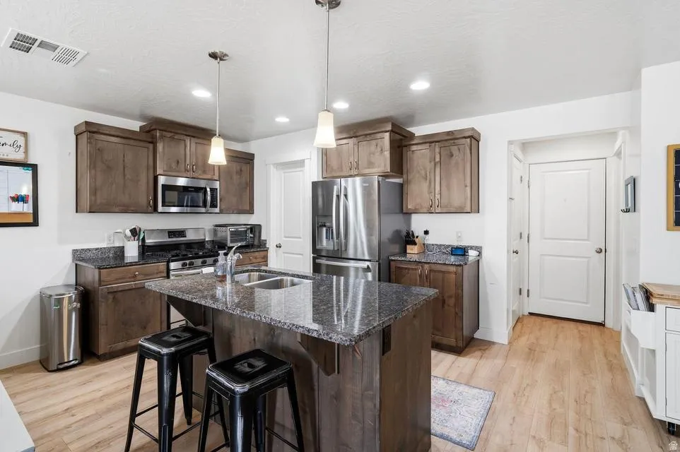 Contemporary kitchen featuring wood-finish cabinetry, stainless steel appliances, and a central island with a double basin sink