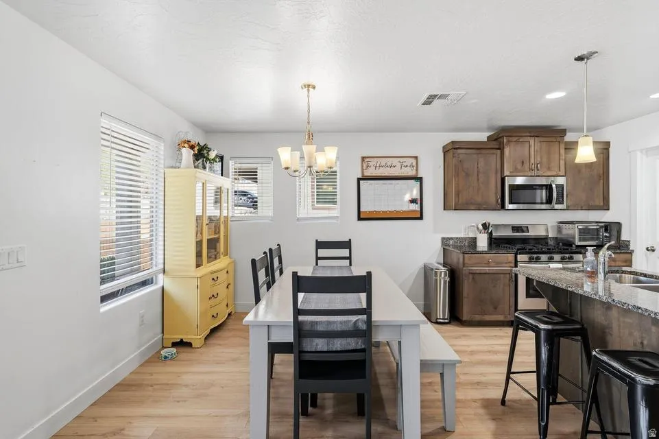 Open-concept kitchen and dining area featuring wood-finish flooring, a kitchen island with seating, dark wood cabinetry, stainless steel appliances, and a dining table with a chandelier