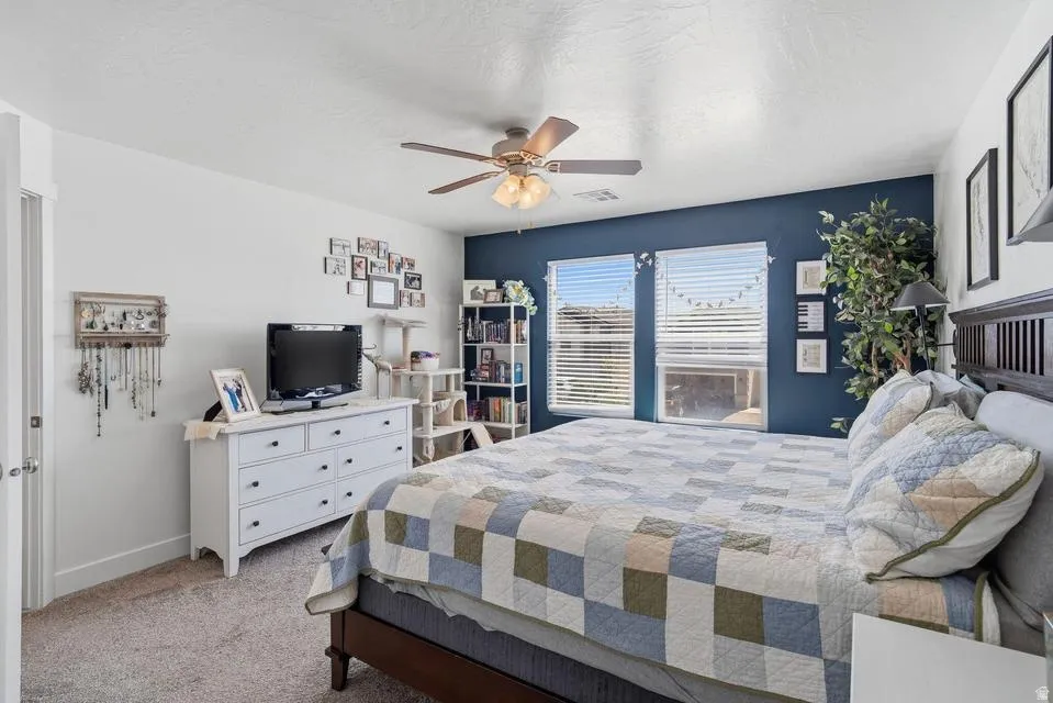 Carpeted room featuring a ceiling fan with integrated lighting, a dark accent wall, and two windows with blinds