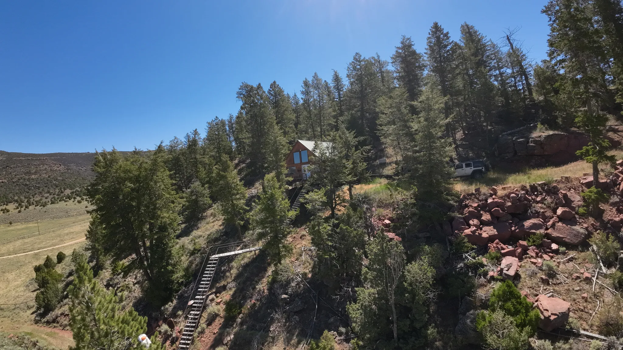 Wood-sided residence situated on a treed hillside with a clear blue sky