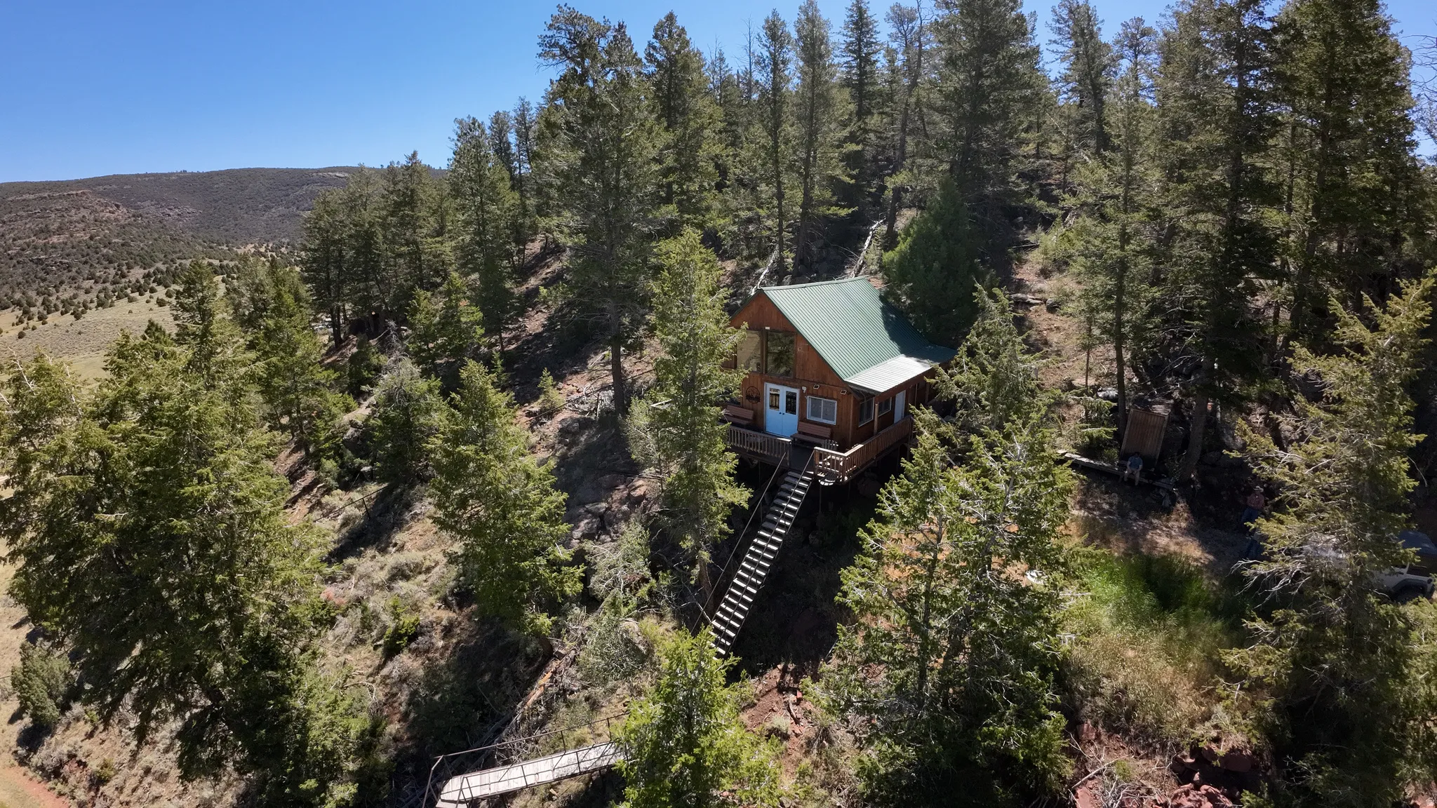 Wood-sided cabin featuring a green metal roof, elevated deck, and extensive wooden staircase