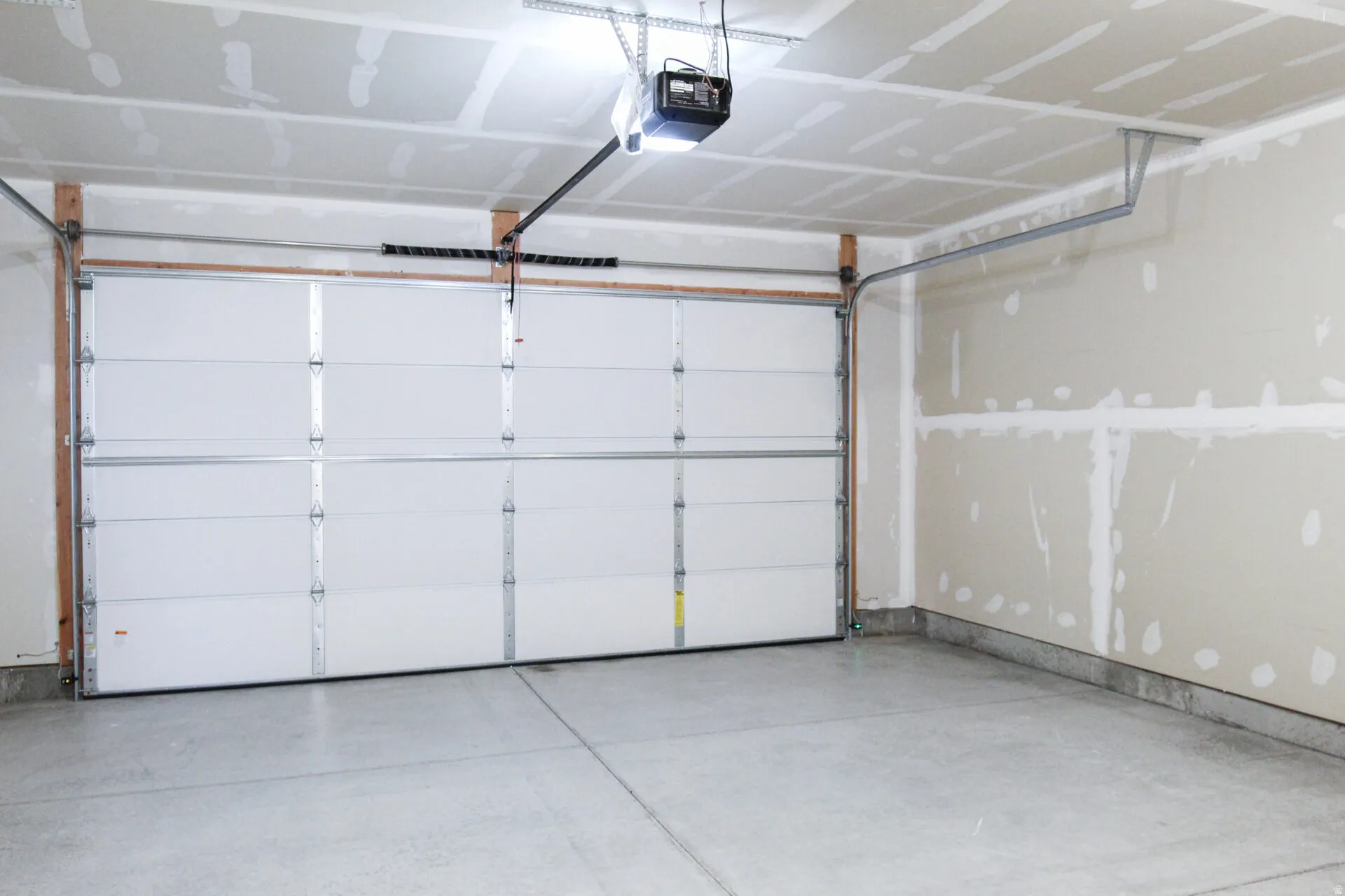 Garage interior featuring a sectional white garage door, overhead garage door opener, concrete flooring, and unfinished drywall walls