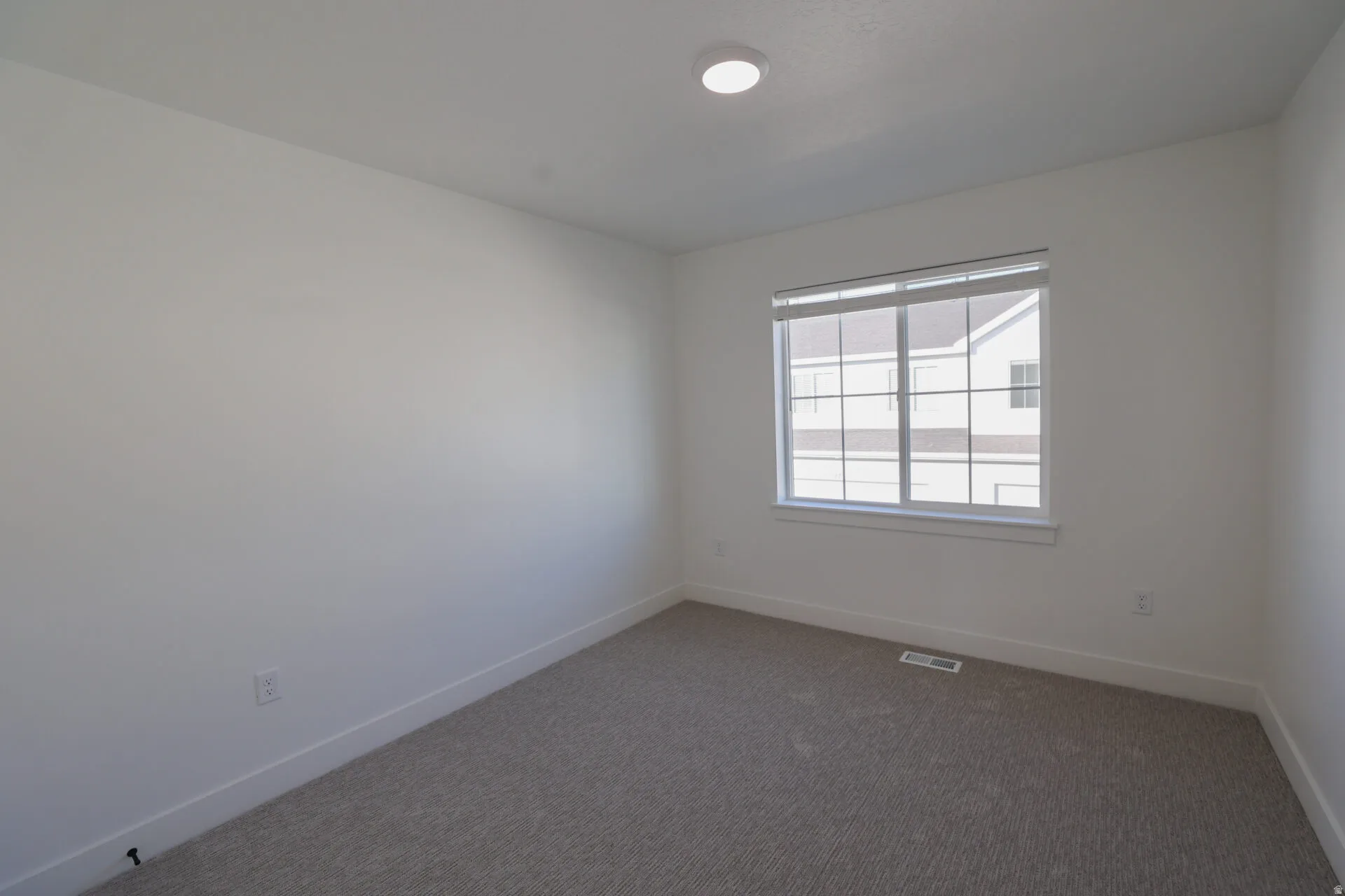 Neutral tone bedroom with a large window, recessed lighting, and grey patterned carpeting
