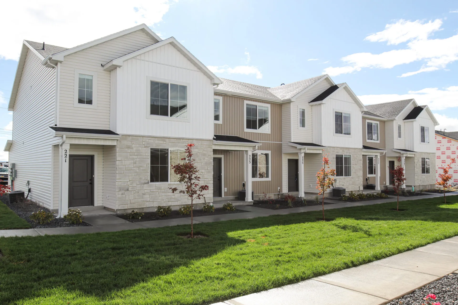 Contemporary townhome-style residences featuring varied neutral siding, stone veneer accents, and dark trim elements