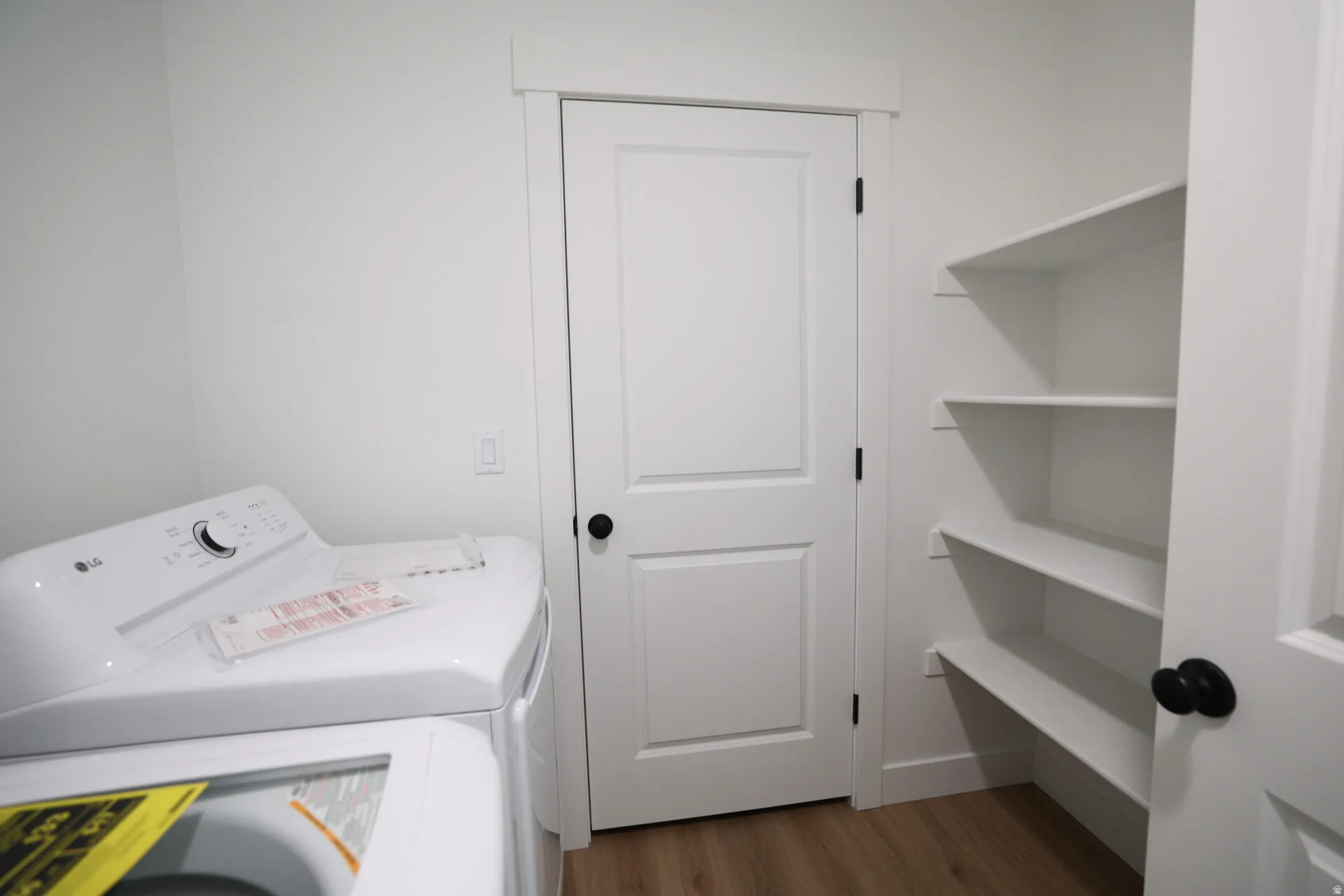 Laundry area featuring wood-finish flooring, white walls, and built-in shelving