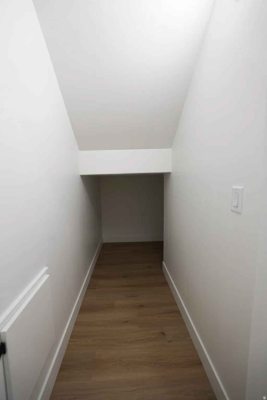 Under-stair storage area featuring wood-finish flooring, white baseboards, and bright white walls