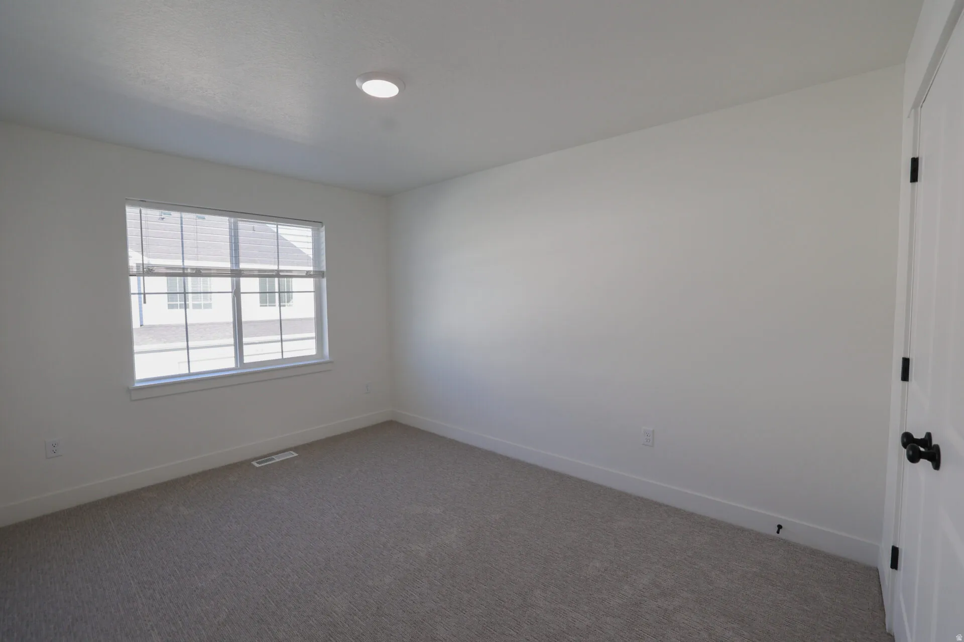 Bedroom featuring neutral-toned carpeting, white walls, and a large window with white blinds