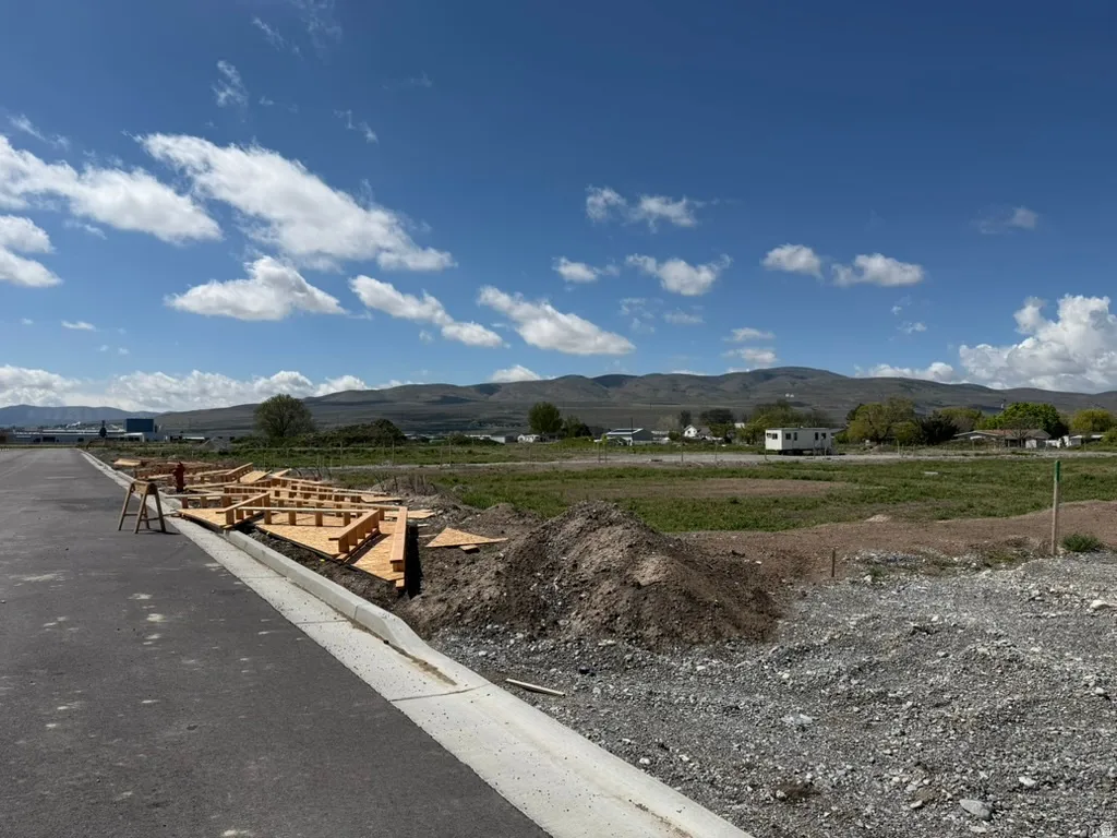 Newly laid asphalt road with a concrete curb and gutter, adjacent to a lot with visible framing for new construction
