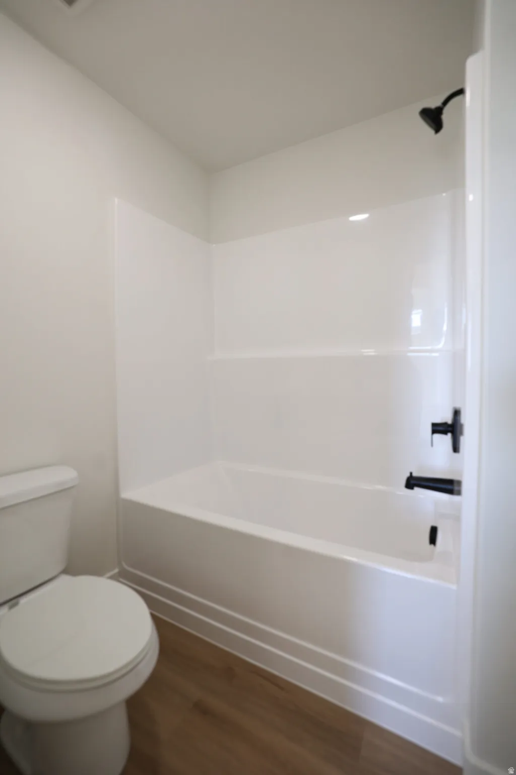 White bathtub with integrated shower, accented by matte black fixtures, set against wood-finish flooring