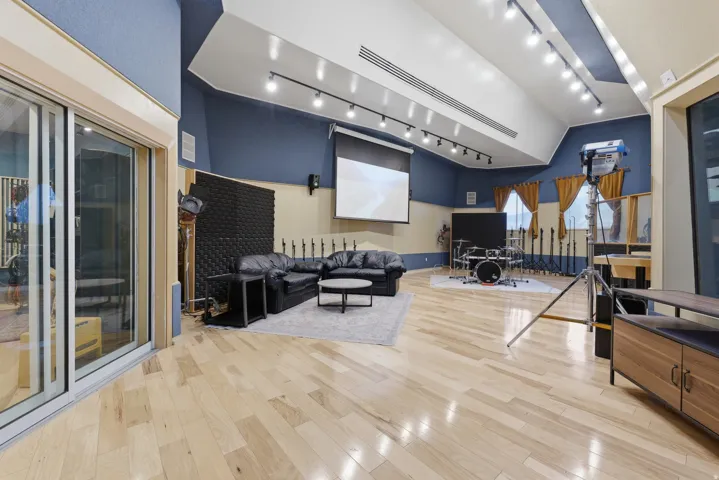Spacious room featuring light wood-finish flooring, a vaulted ceiling with track lighting, and a projection screen