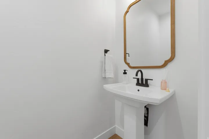Pedestal sink with matte black faucet, framed by a decorative mirror