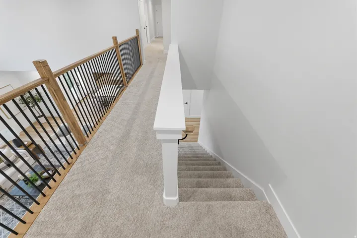 Upper-level hallway featuring light-toned carpeting, a white handrail, and a contemporary wood and black metal baluster system overlooking the lower level